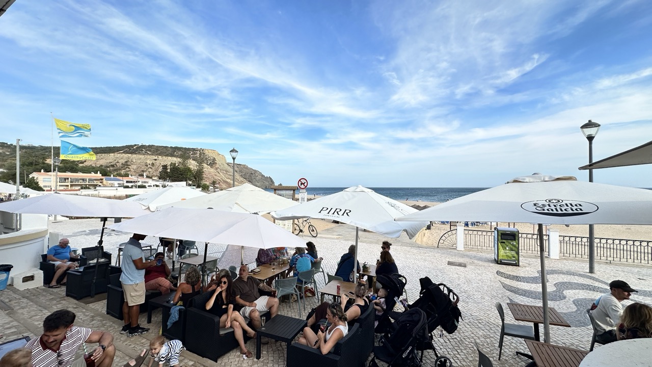 Esplanada com sofás, bandeiras e a falésia da Praia da Luz ao fundo