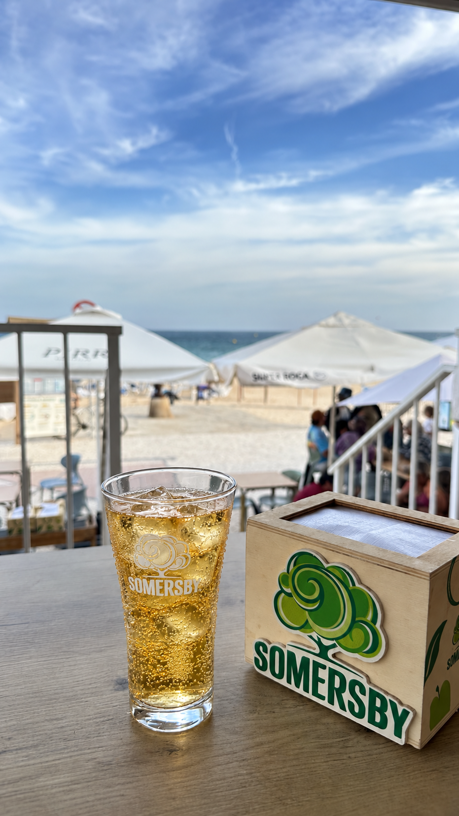 Copo de Somersby na mesa com a esplanada e o mar ao fundo