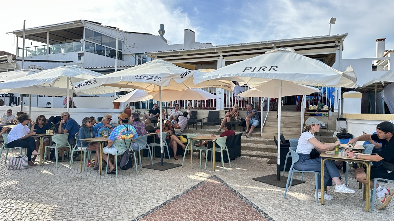 Esplanada cheia com chapéus de sol brancos junto ao restaurante