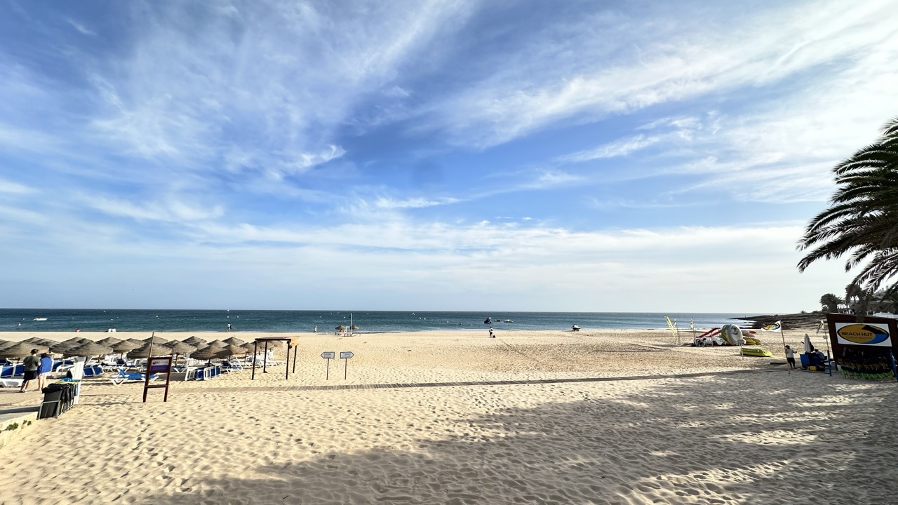 Areal e chapéus de sol da Praia da Luz, no Algarve, com o mar e um céu azul ao fundo